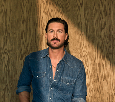 picture of riley green on a denim shirt leaning against a wood wall