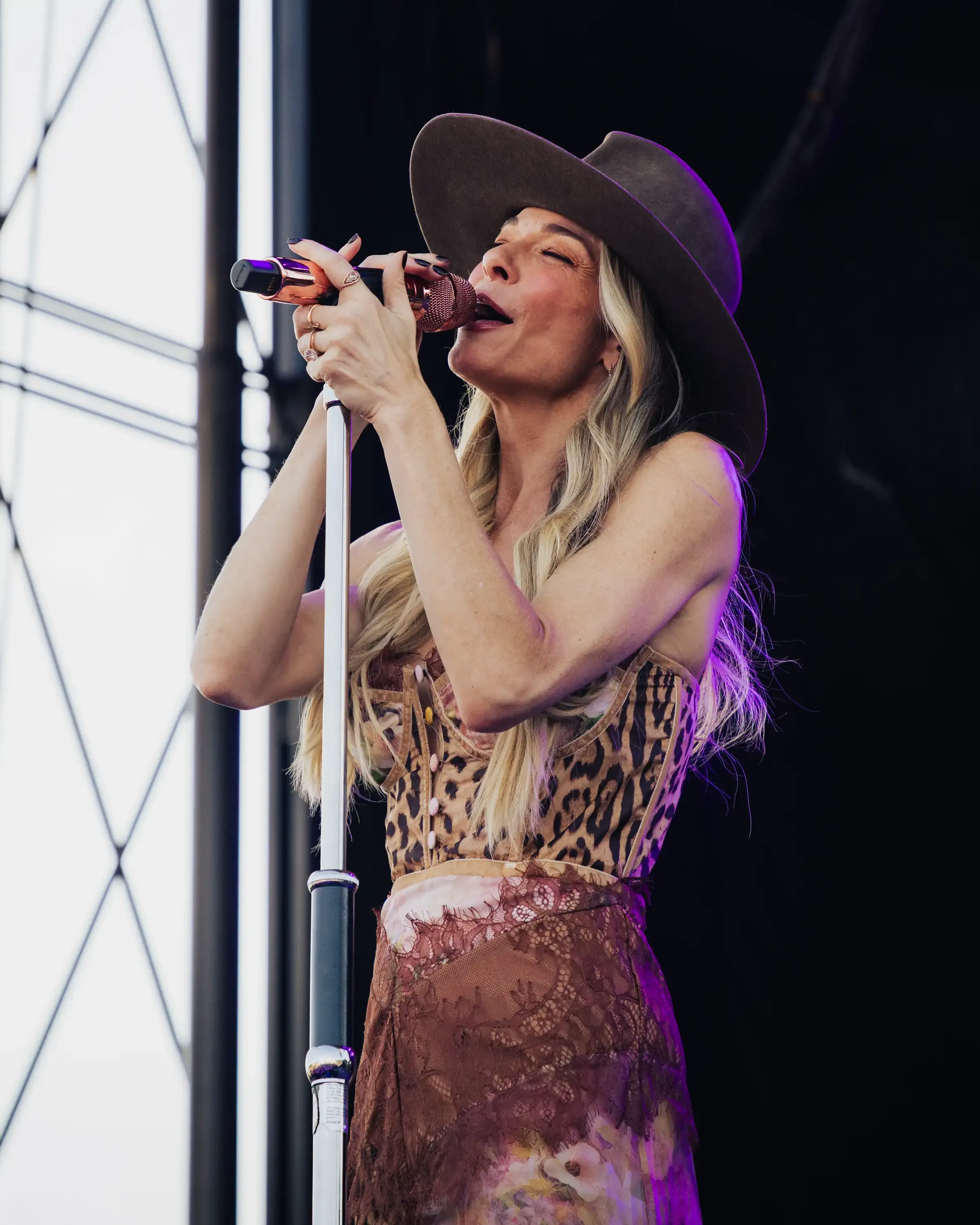 A singer in a wide-brimmed hat at the microphone, lit from the side.
