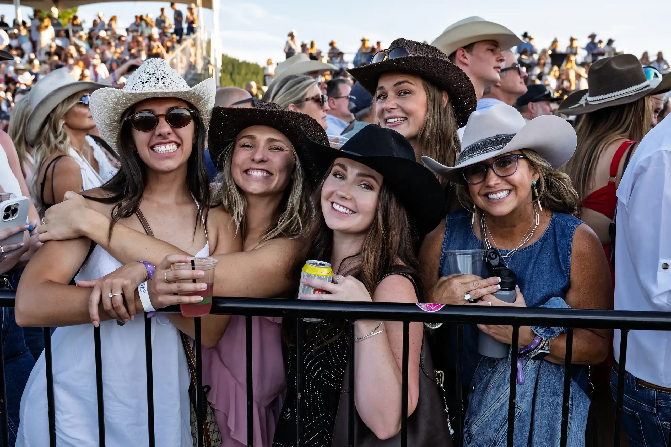 A group of friends in cowboy hats leaning on the front barrier, laughing.