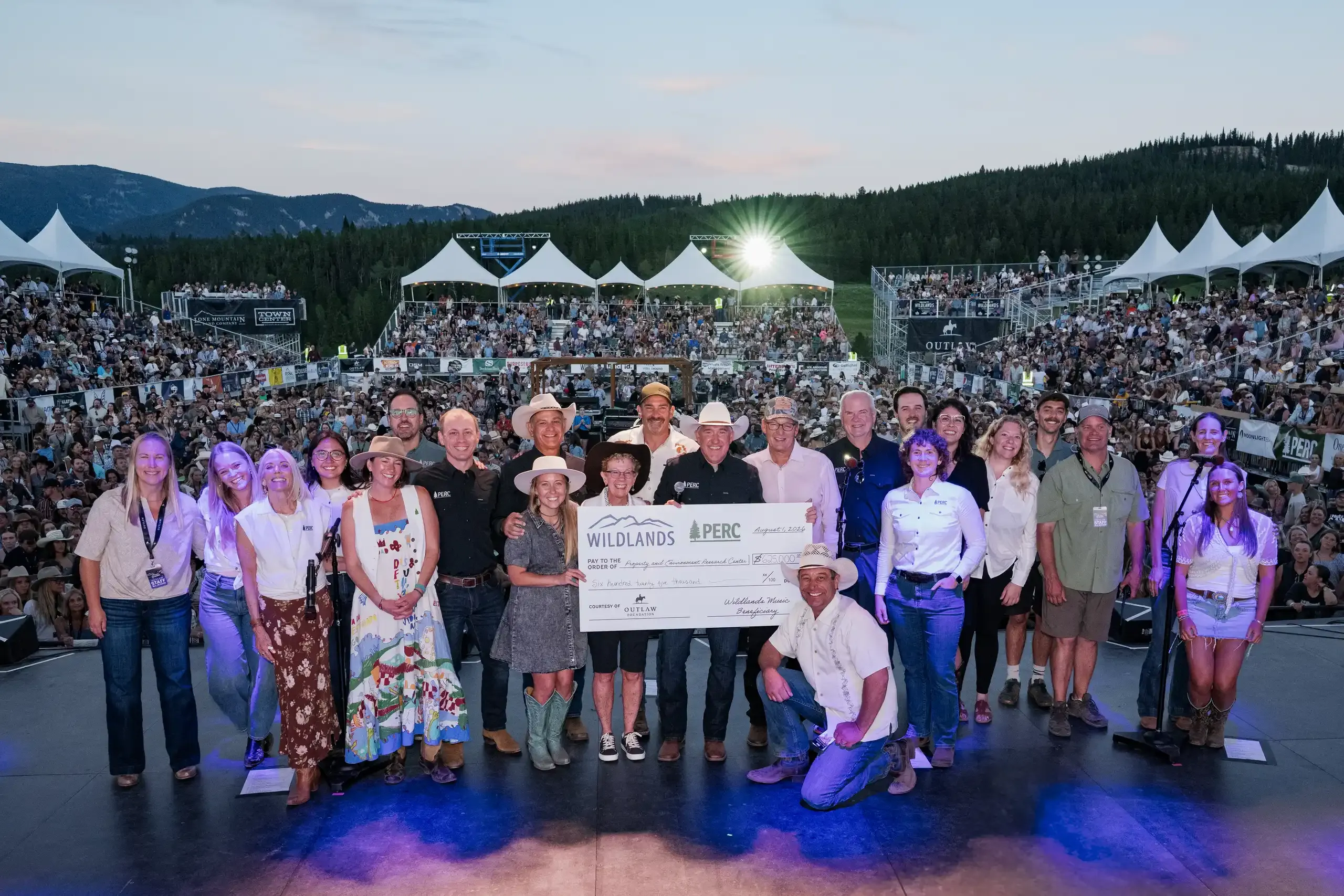 Organisers and conservation partners on stage holding an oversized cheque, with the crowd behind them.