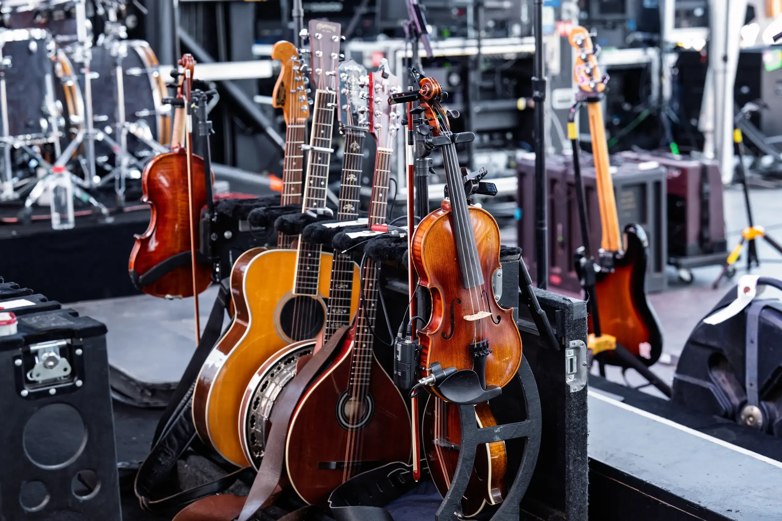 A rack of acoustic guitars and string instruments beside stage equipment.