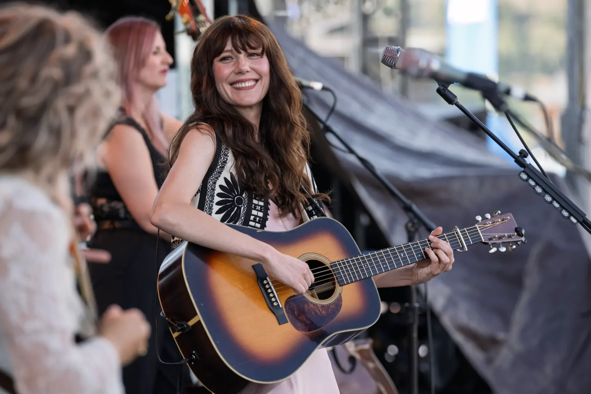 Molly Tuttle at Wildlands. A smiling musician holding an acoustic guitar beside a microphone.
