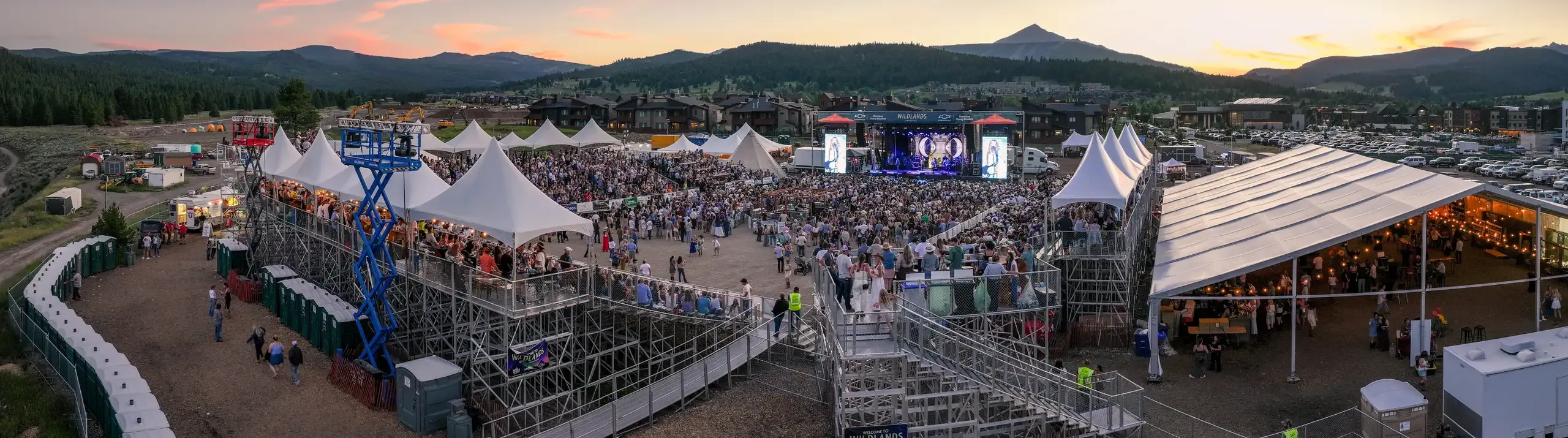 Panoramic aerial view of the festival crowd, tents, and surrounding mountains.