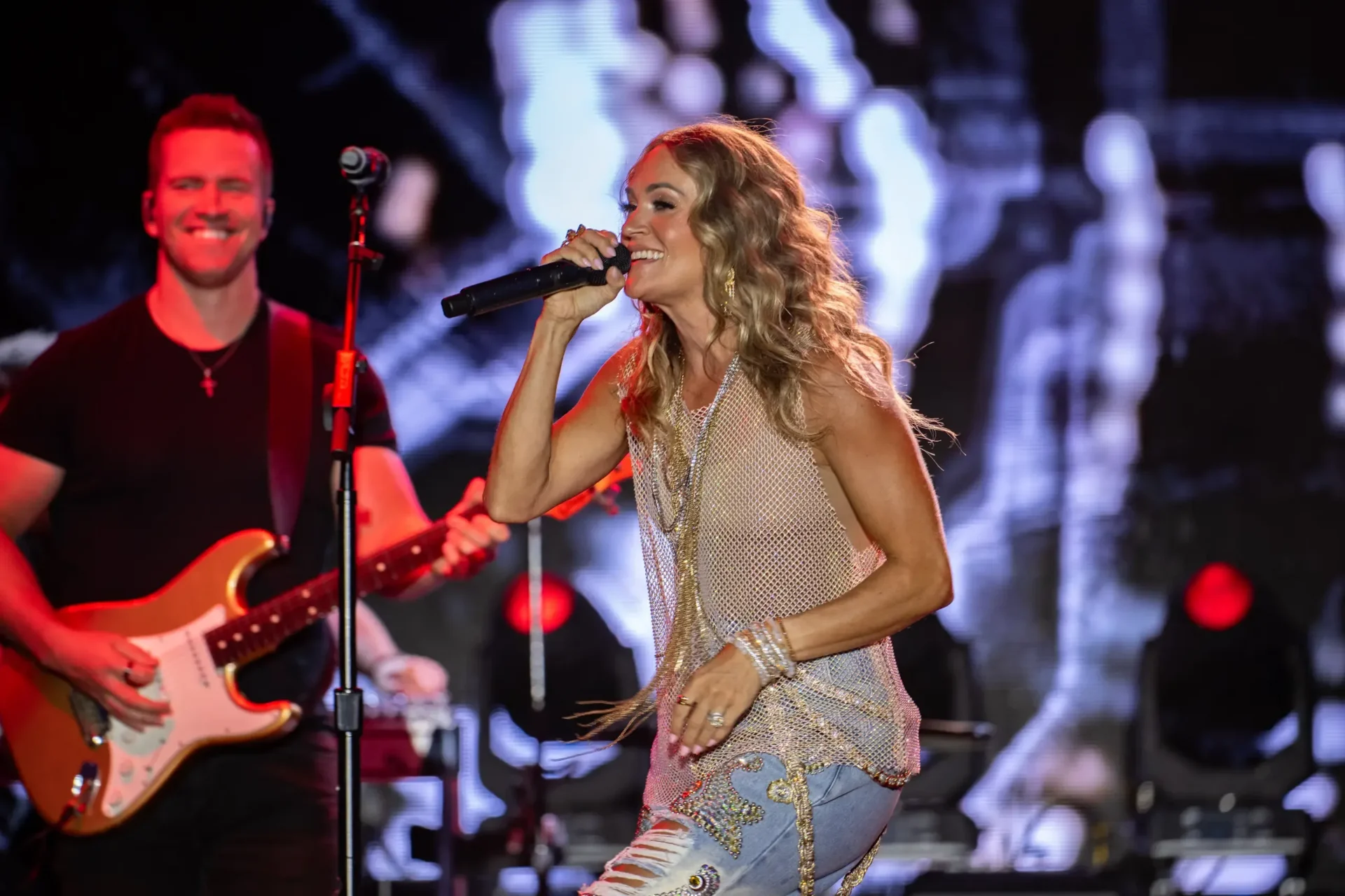 Carrie Underwood at Wildlands. A singer performing into a microphone beside a guitarist under colorful stage lights.